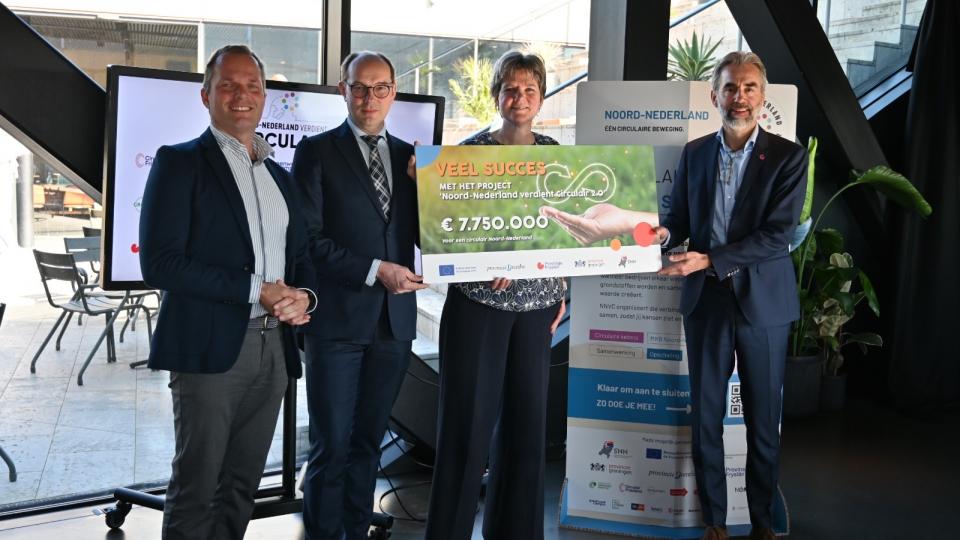 3 mannen en 1 vrouw met een cheque 