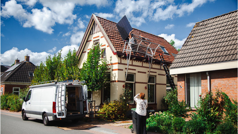 Vrouwelijke woningeigenaar kijkt vanaf de straat hoe zonnepanelen geïnstalleerd worden op haar woning