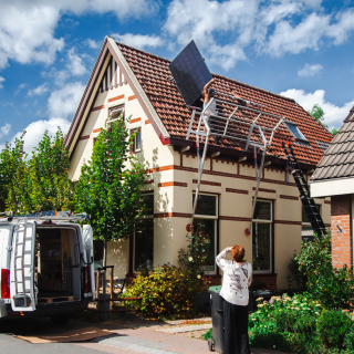 Vrouwelijke woningeigenaar kijkt vanaf de straat hoe zonnepanelen geïnstalleerd worden op haar woning